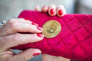 virtueel geld gouden bitcoin op roze vrouwen stoffen portemonnee. vingers met rode nagels op een munt foto