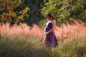 glimlachende zwangere vrouw die zich in kleurrijk gebladerte bevindt