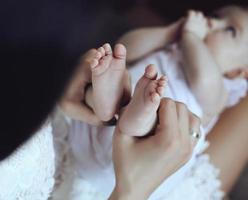 moeder poseren met haar baby, haar voeten in handen houden foto