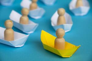 leiderschapsconcept - houten figuur op gele papieren scheepsorigami die de rest van de figuur op wit papieren schip leidt. foto