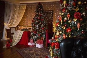 kerstinterieur van de donkere woonkamer van het huis. kerstboom, lampjes van slingers aan de muren, bibliotheekkast, boeken op de planken. luxe interieur. nieuwjaar, rode en gouden ballen. foto