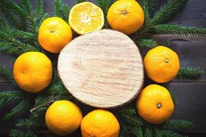 nieuwjaarsvakantie achtergrond op ronde snede van boom omringd door mandarijnen, levende dennentakken en gouden lichtslingers, met houten ruimte voor tekst. citrusaroma, schijfjes sinaasappel, kerstmis. kader foto