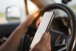de hand van de bestuurder achter het stuur houdt een smartphone vast. navigator, satellietnavigatie, communicatie in de auto, verkeersveiligheid, speakerphone foto