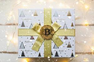 een bitcoin-munt op een doos met een cadeau voor kerstmis en nieuwjaar. cryptocurrency, financiën, rijkdom en beleggen. kerstverlichting, wenskaart foto