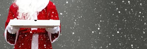 witte pizzadoos in handen van de kerstman in wanten, met een baard, in een rode jas. kerst fastfood levering. nieuwjaarsactie. werken op feestdagen catering. kopieer ruimte, bespotten. banier foto