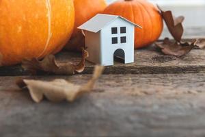 herfst achtergrond. speelgoed huis en pompoen op houten achtergrond. Thanksgiving banner kopie ruimte. hygge mood, verandering van seizoenen concept. hallo herfst met halloween-familiefeest. foto