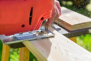 houtbewerker die houten paneel snijdt met decoupeerzaag buitenshuis, vergrote weergave van man aan het werk met elektrische decoupeerzaag en houten plank foto