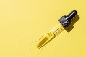 fles pipet druppelaar met vloeibare gele retinol of vitamine c gel of serum op een gele achtergrond. huidverzorging uitstrijkje foto