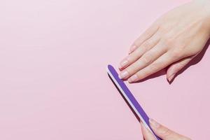 vrouw vijlt haar nagels met paarse fimger-vijl, maakt manicure thuis, handenverzorging, tijd voor jezelf concept. roze achtergrond. bovenaanzicht foto