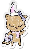 schattige, verontruste stickercartoon van een kat met een cadeautje met een kerstmuts vector
