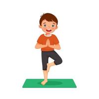 kleine jongen doet gymnastische fitnessoefeningen die yoga beoefenen op een groene mat binnen thuis vector