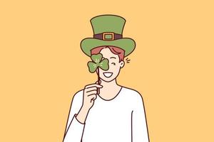 gelukkig Mens met st Patrick dag viering accessoires vervelend groen hoed en aan het bedekken oog met Klaver bloemblad. positief vent nodigt uit naar traditioneel festival Aan vooravond van Iers vakantie st Patrick dag vector