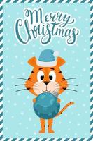een schattige cartoontijger met een kerstmuts staat en houdt een ronde blauwe kerstboom vast. wenskaart met hand belettering vrolijk kerstfeest. kleur vectorillustratie op een blauwe achtergrond met sneeuwvlokken. vector