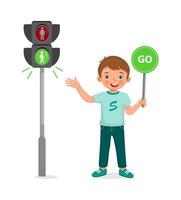 schattige kleine jongen die een bord vasthoudt in de buurt van een voetgangersverkeerslicht met een groen indicatielampje aan vector