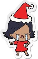 Aufkleberkarikatur eines Mädchens, das weint und mit Weihnachtsmütze zeigt vektor