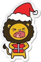 Aufkleber Cartoon eines Löwen mit Weihnachtsgeschenk mit Weihnachtsmütze vektor