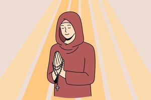 religion och andlig tro begrepp. ung leende kvinna nunna med ögon stängd i huva stående med händer korsade och bön- i stråle av ljus vektor illustration