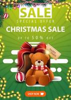 Sonderangebot, Weihnachtsverkauf, bis zu 50 Rabatt, grünes vertikales Banner mit Weihnachtsbaumzweigen, Girlanden, Knopf und Geschenk mit Teddybär vektor