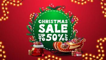 Weihnachtsverkauf, bis zu 50 Rabatt, vertikales rotes Rabattbanner mit grünem Kreis mit Angebot, verziert mit Weihnachtsbaumzweigen, Süßigkeiten und Girlanden sowie Weihnachtsmannschlitten und Tasche mit Geschenken vektor