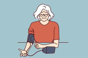 äldre kvinna användningar tonometer till mäta blod tryck och kolla upp för symptom av hypertoni. gråhårig mormor oberoende av åtgärder blod tryck, tar vård av egen hälsa vektor