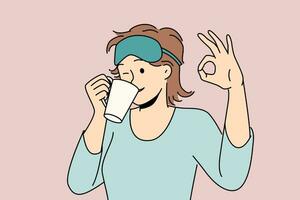 kvinna drycker morgon- kaffe efter vakna upp och visar ok gest stående i sömn mask och pyjamas. flicka blinkar njuter varm kaffe eller te dryck till heja på upp och skaffa sig redo för arbete dag vektor