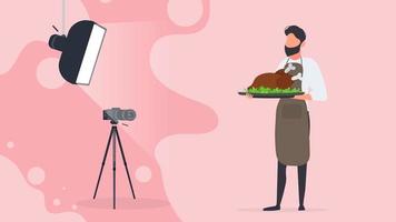 kulinarische Bloggerin. Ein Mann in einer Küchenschürze hält ein Brathähnchen auf einem Tablett. Kamera auf Stativ, Softbox. kulinarischer Blog oder Vlog-Konzept. Vektor. vektor