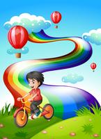 Ein Junge, der am Hügel mit einem Regenbogen radfährt vektor