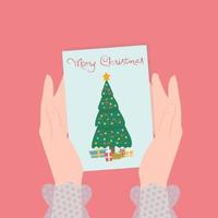 frauenhände halten eine karte mit einem weihnachtsbaum und geschenken und der aufschrift frohe weihnachten. vektor