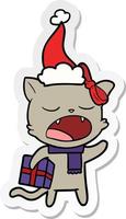 klistermärke tecknad av en katt med julklapp bär tomte hatt vektor
