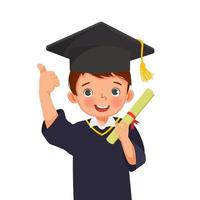 söt liten skolpojke i examen hatt och klänning håller diplom certifikat tummen upp vektor