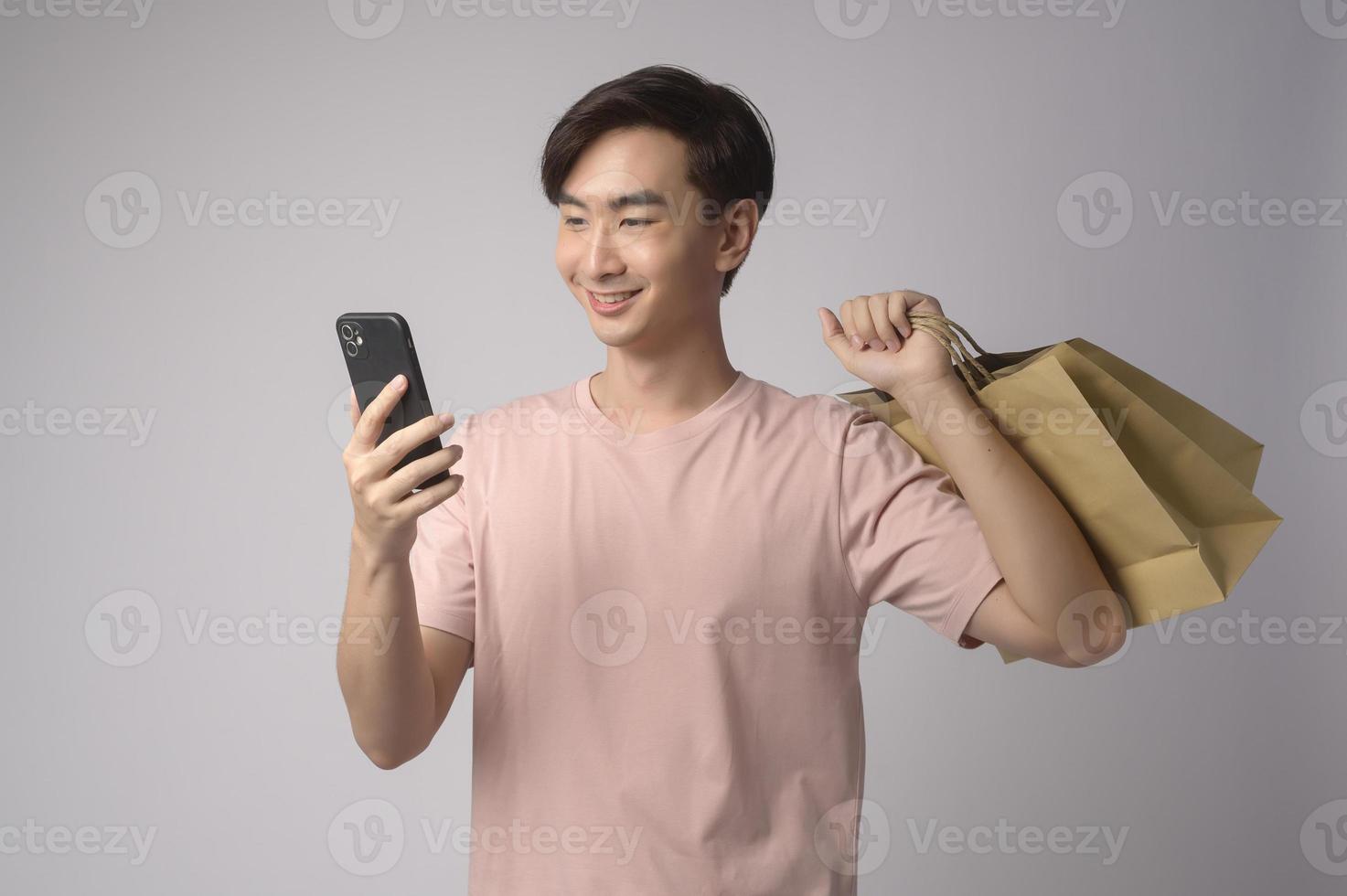 jeune homme asiatique tenant un smartphone et un sac à provisions sur fond blanc concept de studio, de shopping et de finance. photo