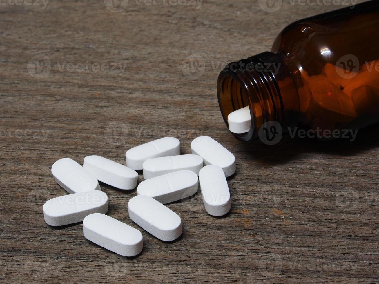 pilules débordant d'une bouteille de pilules sur table en bois photo