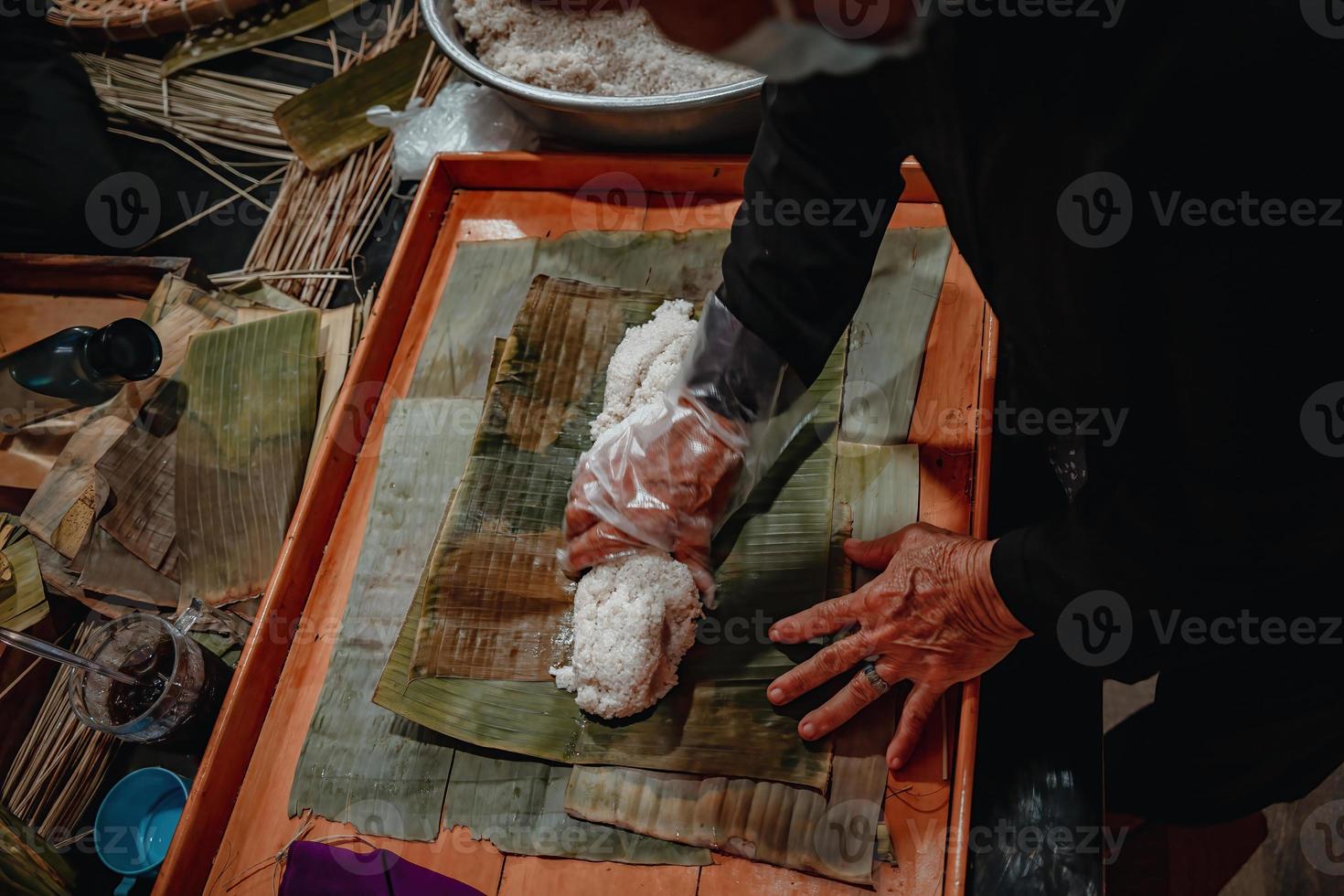 focus vieille femme avec une robe traditionnelle vietnamienne ao ba ba faisant, enveloppant le gâteau tet, la nourriture tet du nouvel an lunaire vietnamien en plein air à la main. photo