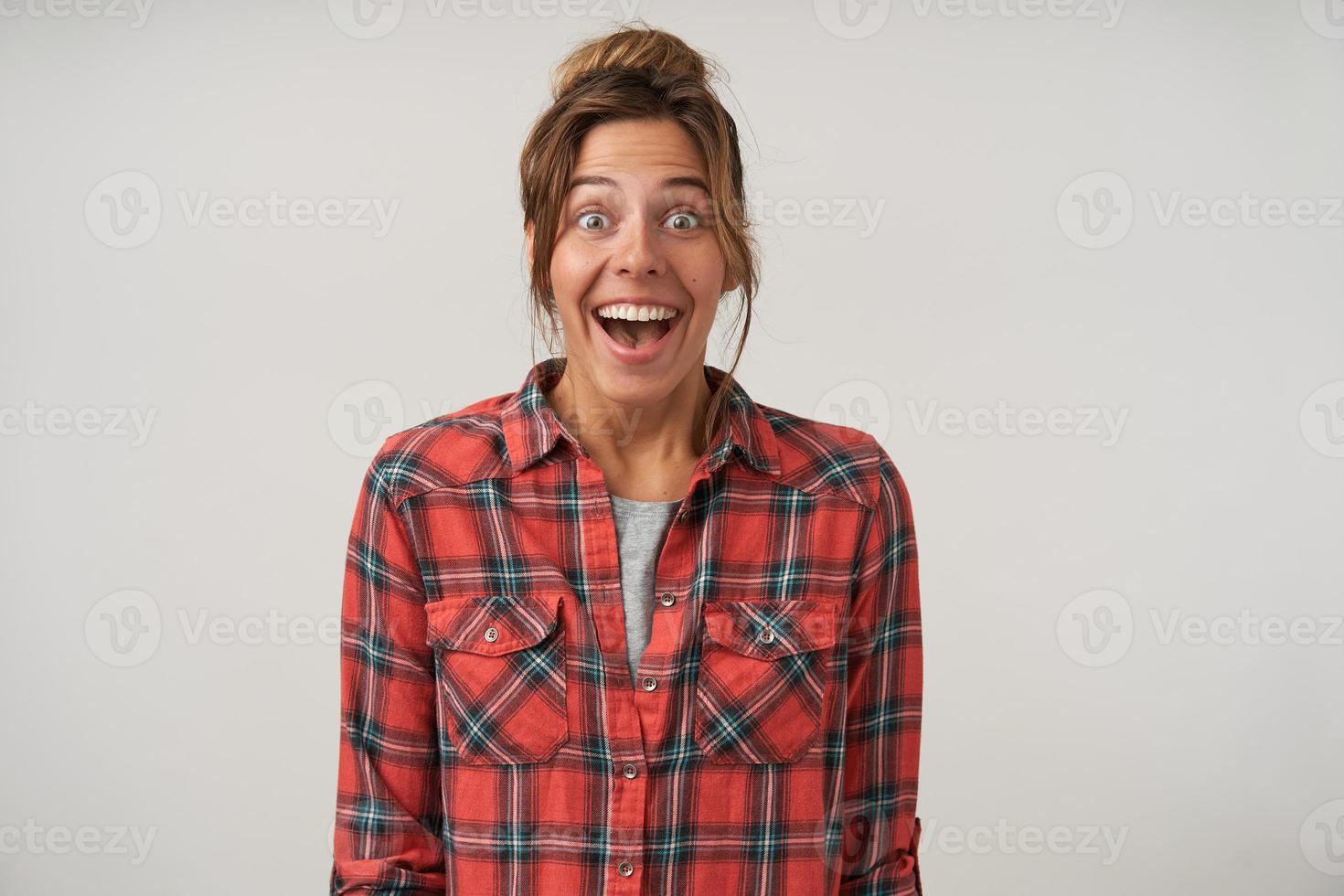 prise de vue en studio d'une jolie jeune femme surprise en chemise à carreaux, souriant largement à la caméra avec une coiffure décontractée et un maquillage naturel, isolée sur fond blanc photo