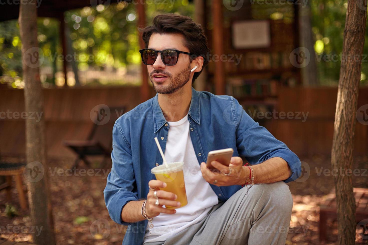 portrait d'un jeune homme barbu séduisant avec une tasse de thé glacé à la main, regardant au loin photo