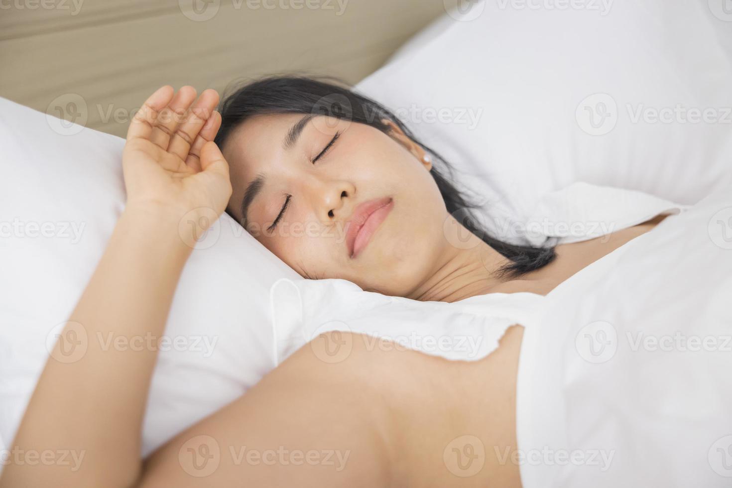 jeune femme asiatique dormant dans son lit dans la chambre. elle est allongée sur le côté et se détend les yeux fermés photo