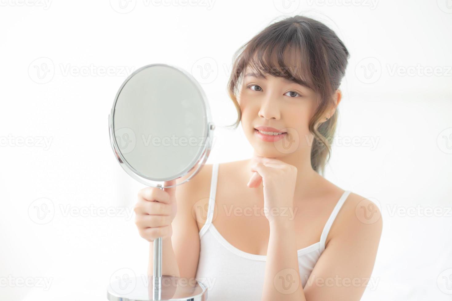 beau visage jeune femme asiatique avec un sourire heureux et un miroir à la recherche, maquillage de beauté faciale fille avec soins de la peau et traitement cosmétique, rafraîchissement de la femme et propre pour un concept charmant et sain. photo