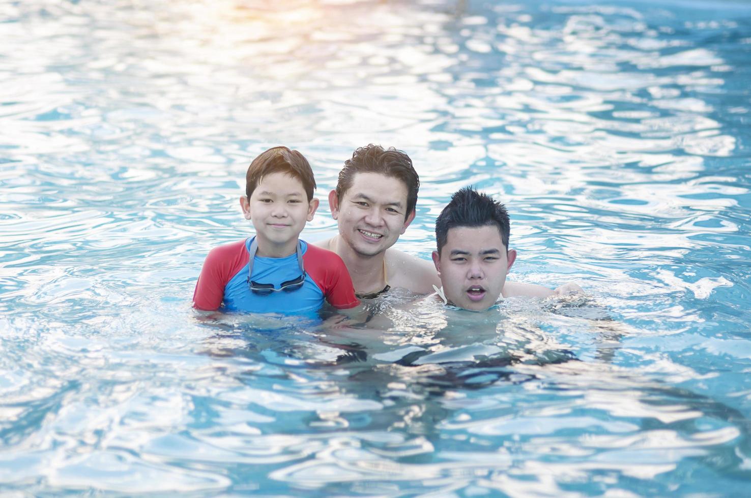 père et ses deux fils jouent dans une piscine d'eau claire - concept de temps de jeu en famille heureuse photo
