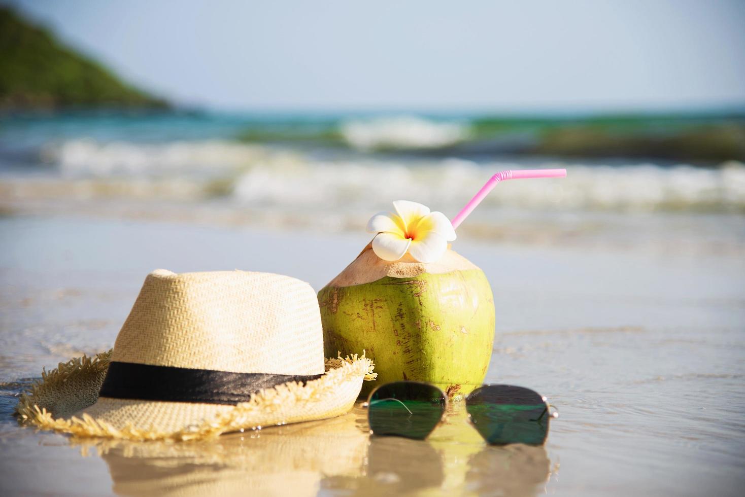 noix de coco fraîche avec chapeau et lunettes de soleil sur une plage de sable propre avec fond de vague de mer - fruits frais avec concept de fond de vacances au soleil de sable de mer photo