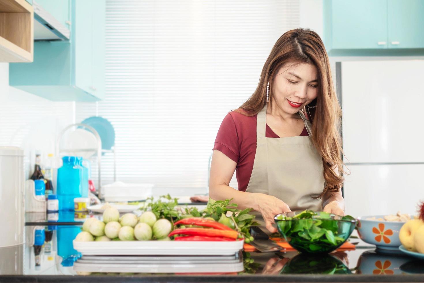 jeune femme dans une cuisine moderne et lumineuse prépare des aliments avec des légumes colorés - les gens et la maison font le concept d'activité de cuisine photo