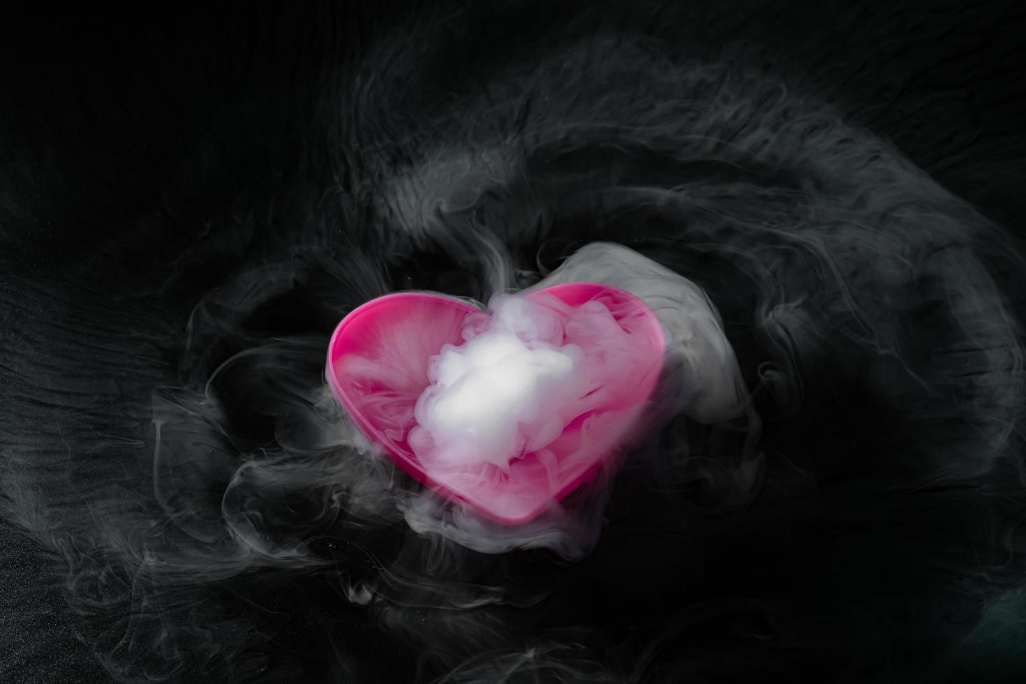 fumée de glace carbonique avec tasse en forme de coeur rose isolée sur fond noir photo