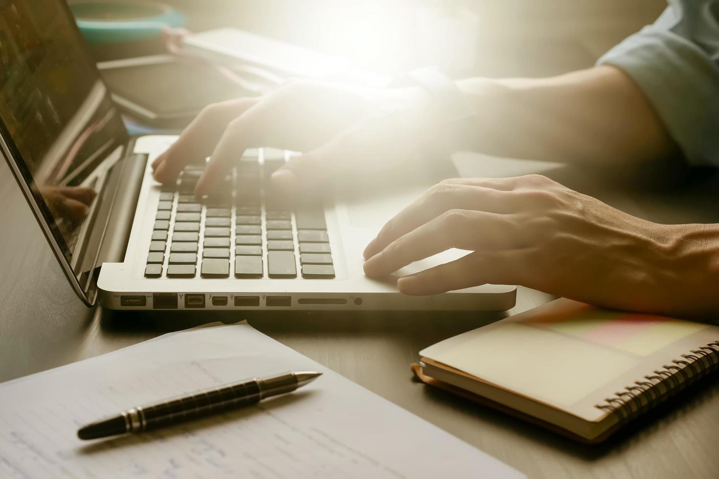 gros plan de mains masculines travaillant sur un ordinateur portable sur son bureau, tonique avec la lumière du soleil. photo