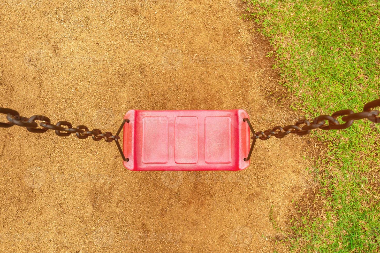 prenez une vue de dessus de la balançoire rouge avec des chaînes dans la cour de récréation. dans le parc vu le sol et l'herbe photo