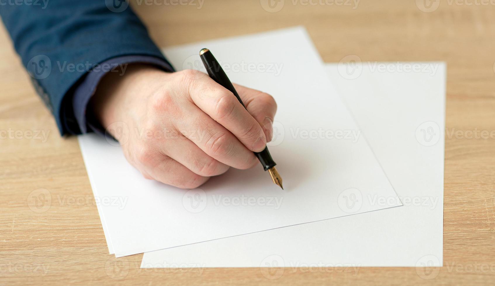 gros plan de la main d'un homme d'affaires en costume, écrivant une lettre ou signe un document sur un morceau de papier blanc avec un stylo plume avec plume photo