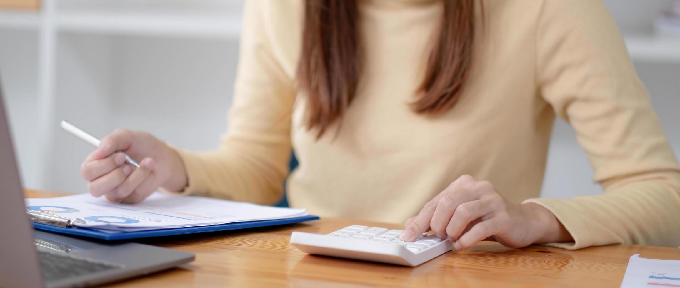 femme d'affaires en gros plan à l'aide d'une calculatrice et d'un ordinateur portable pour faire des finances mathématiques sur un bureau en bois dans un bureau et des antécédents de travail, fiscalité, comptabilité, statistiques et concept de recherche analytique photo