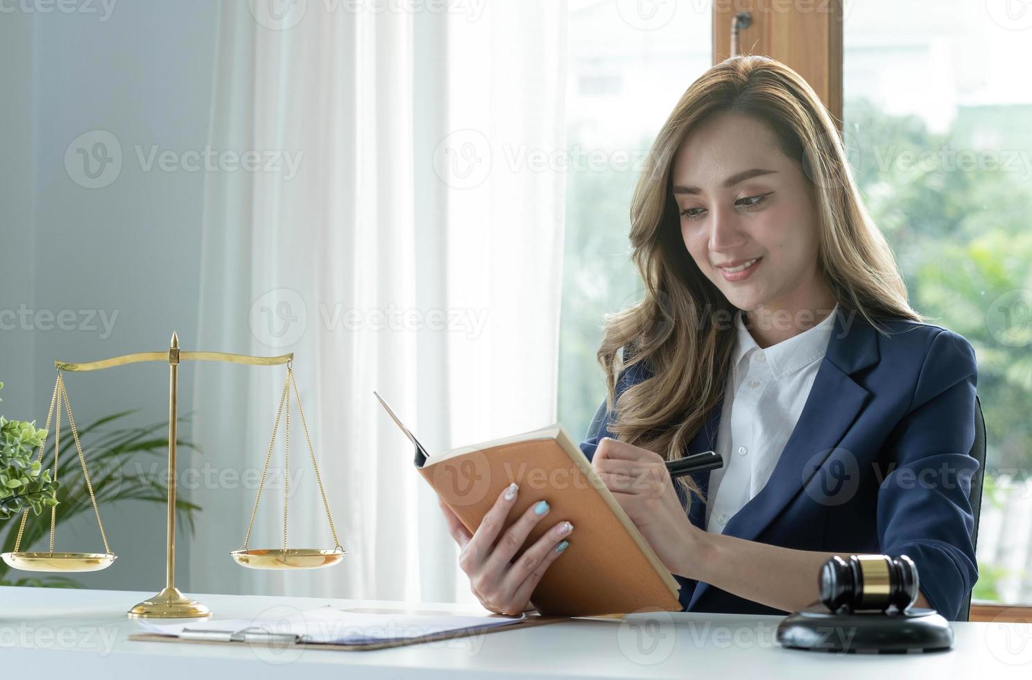 jeune avocate asiatique confiante et prospère ou consultante juridique en affaires lisant un livre de droit ou écrivant quelque chose sur son cahier à son bureau. photo