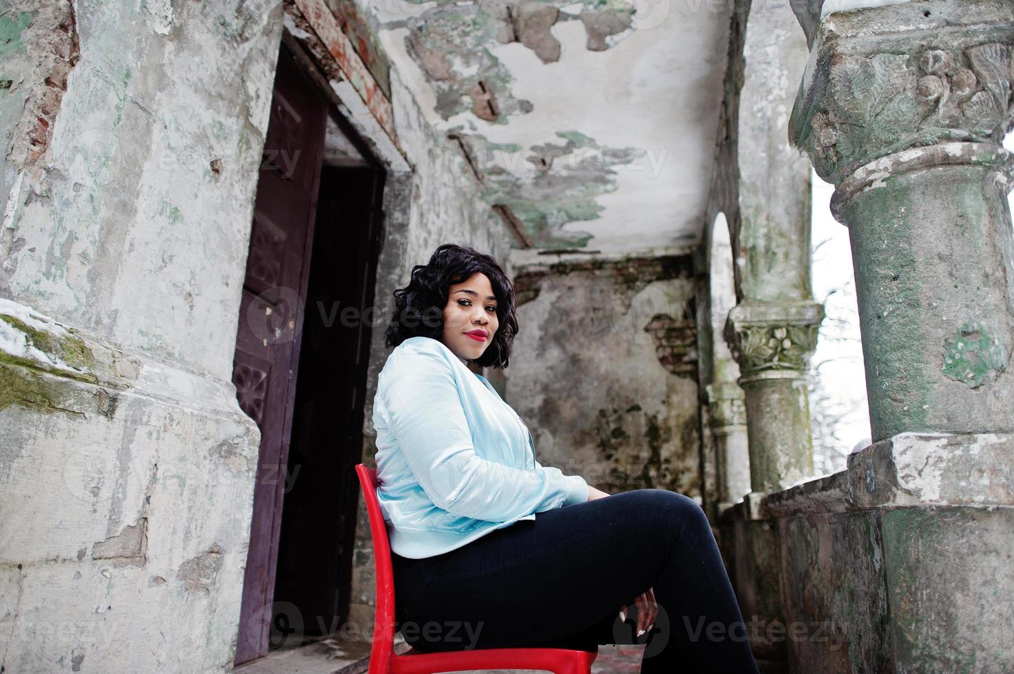 élégant modèle de taille plus afro-américain assis sur une chaise rouge en plein air. photo