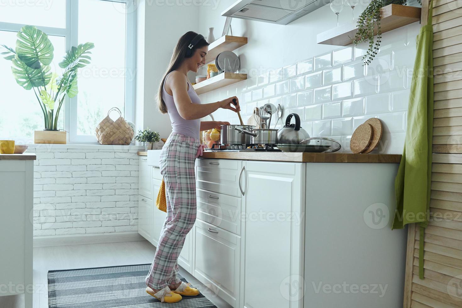 toute la longueur d'une jeune femme au casque écoutant de la musique tout en cuisinant à la cuisine photo