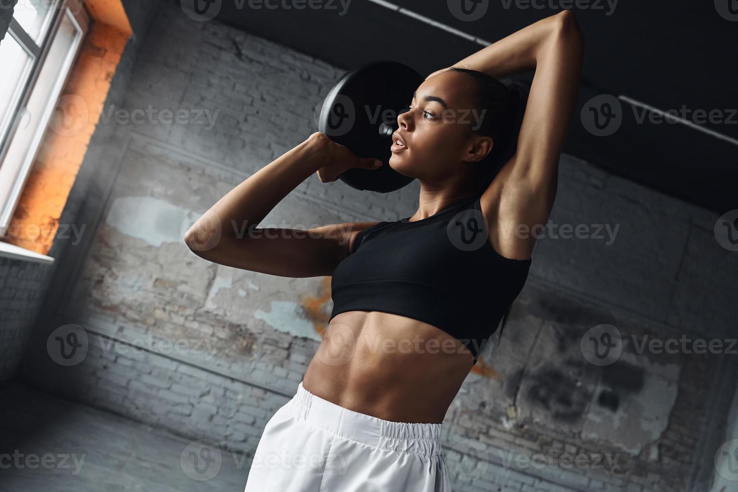 confiante jeune femme africaine travaillant avec des poids tout en faisant de l'exercice dans une salle de sport photo