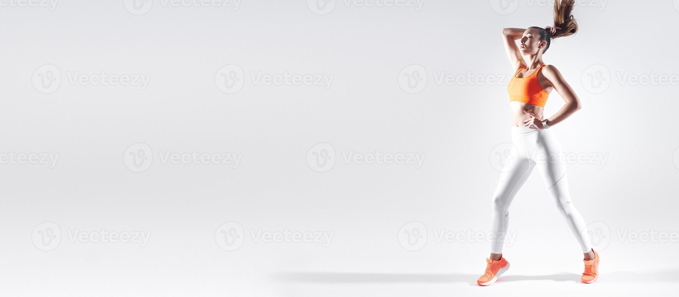 jeune femme confiante en vêtements de sport ajustant ses cheveux sur fond blanc photo
